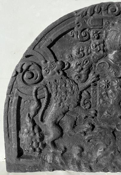A semicircular cast iron fireplace plaque, decorated with a coat of arms, surmounted by a helmet and framed by lions.-1