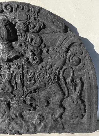 A semicircular cast iron fireplace plaque, decorated with a coat of arms, surmounted by a helmet and framed by lions.-5